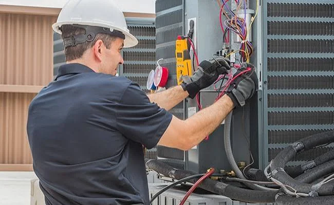 HVAC technician inspecting wiring inside a large outdoor condenser