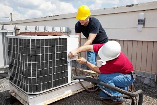 Two HVAC technicians working on an outdoor air conditioning system
